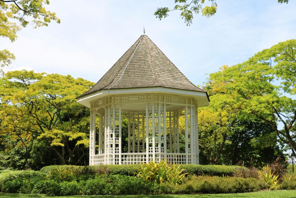 A picturesque white gazebo surrounded by vibrant green trees and well-manicured bushes.