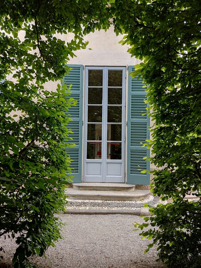 Elegant French door framed by lush greenery and pebble pathway.